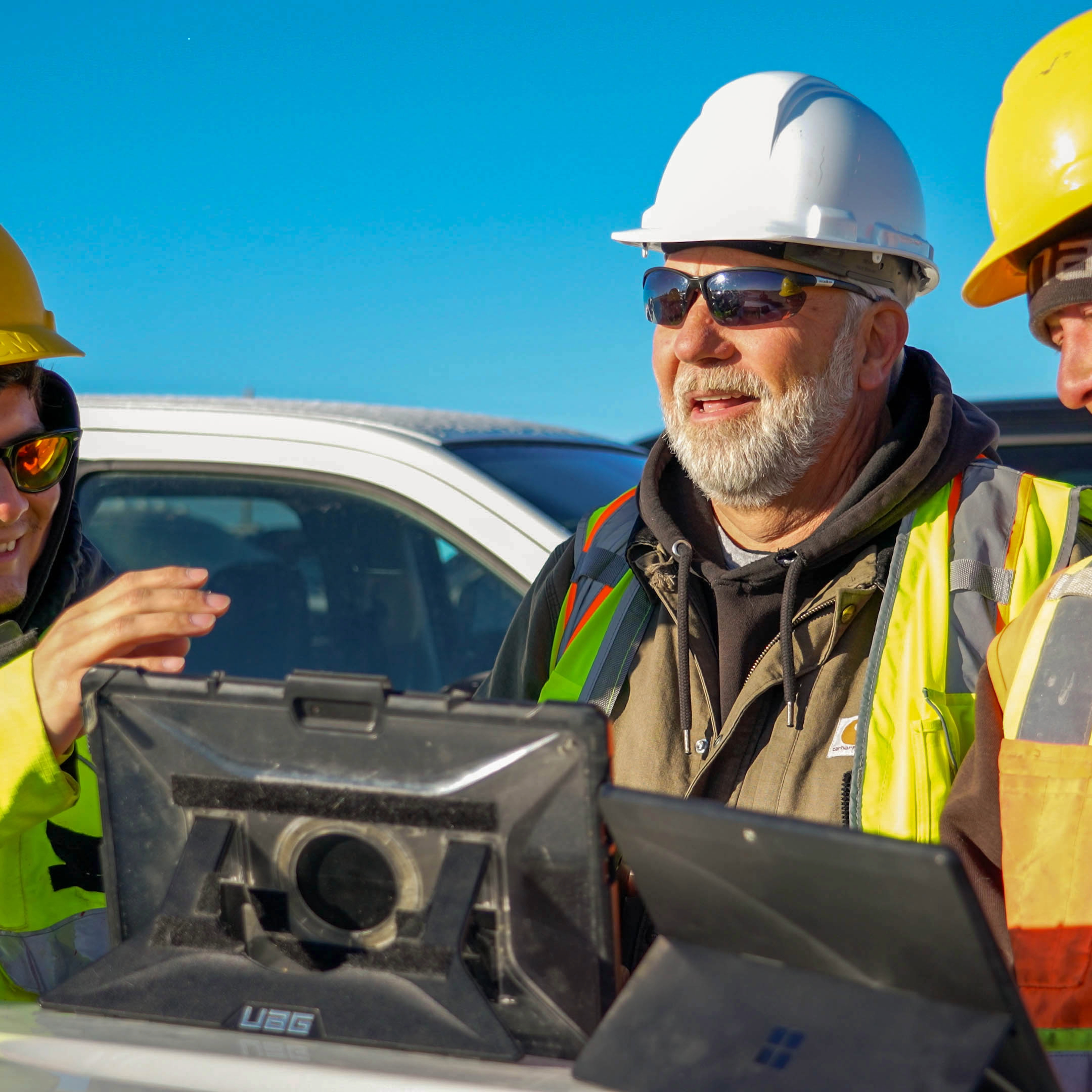 Man looking at computer, wearing a hard hat on a job site